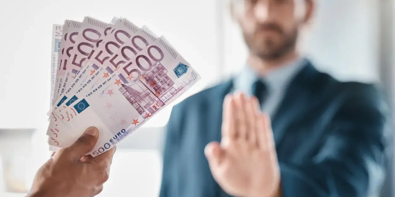 Ręka podaje plik banknotów 500 euro. Mężczyzna w garniturze odrzuca ofertę, mówiąc, że klient nie zapłacił za usługę.