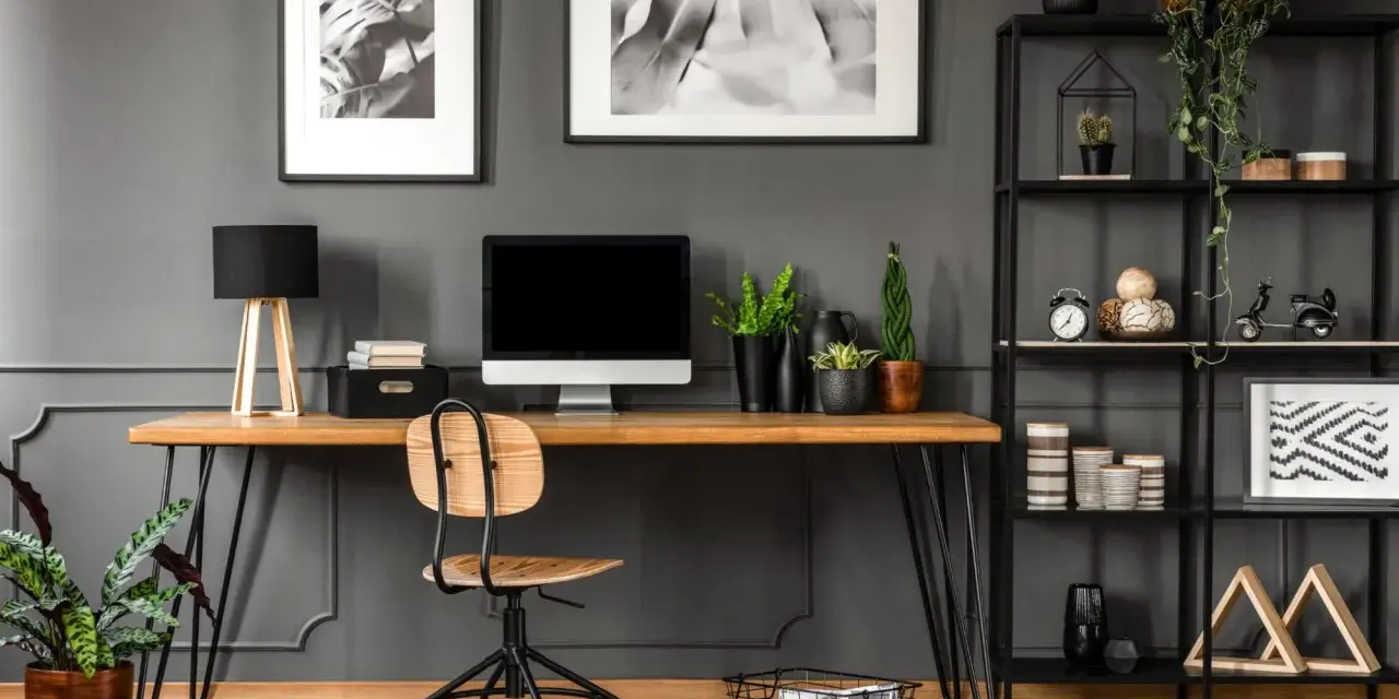 Arredamento studio casa: scrivania in legno con computer, sedia, piante e libreria nera piena di oggetti decorativi.