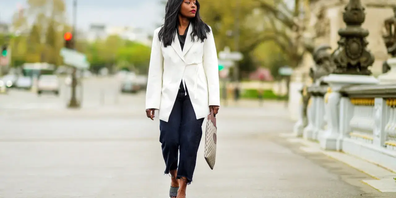 Mujer con un look smart elegant, lleva un blazer blanco, jeans oscuros y sandalias de diseño.