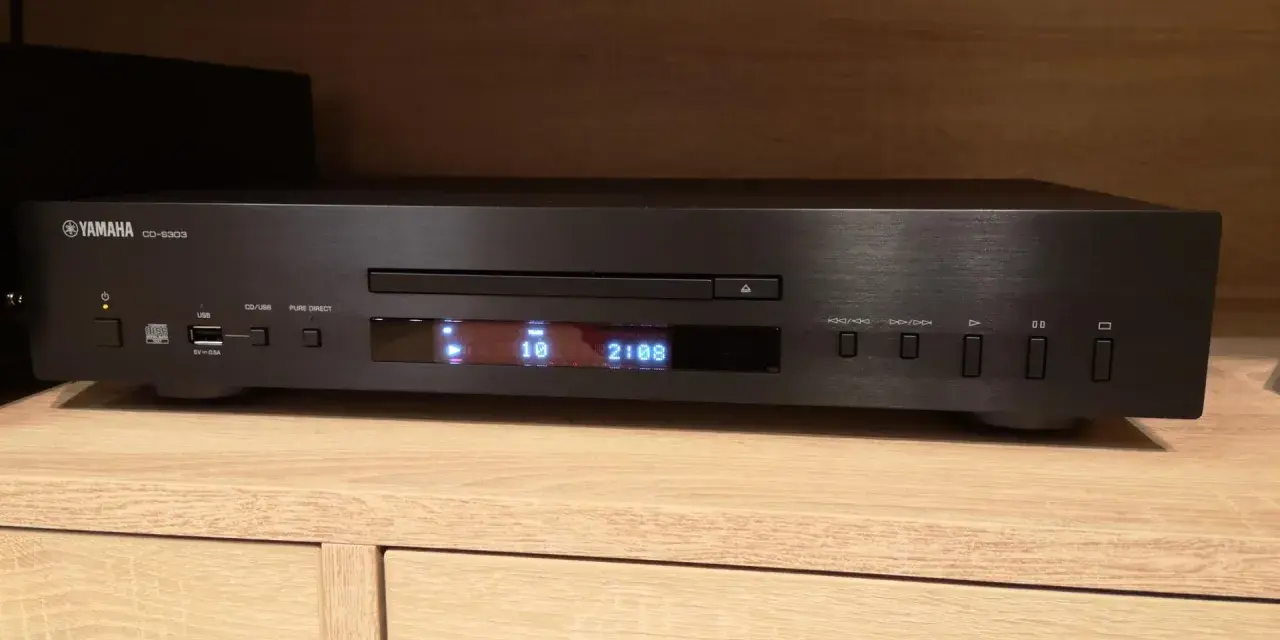 Czarny odtwarzacz CD Yamaha CD-S303 na drewnianej półce, gotowy do testu. Wyświetlacz pokazuje utwór 10 z 2:08.