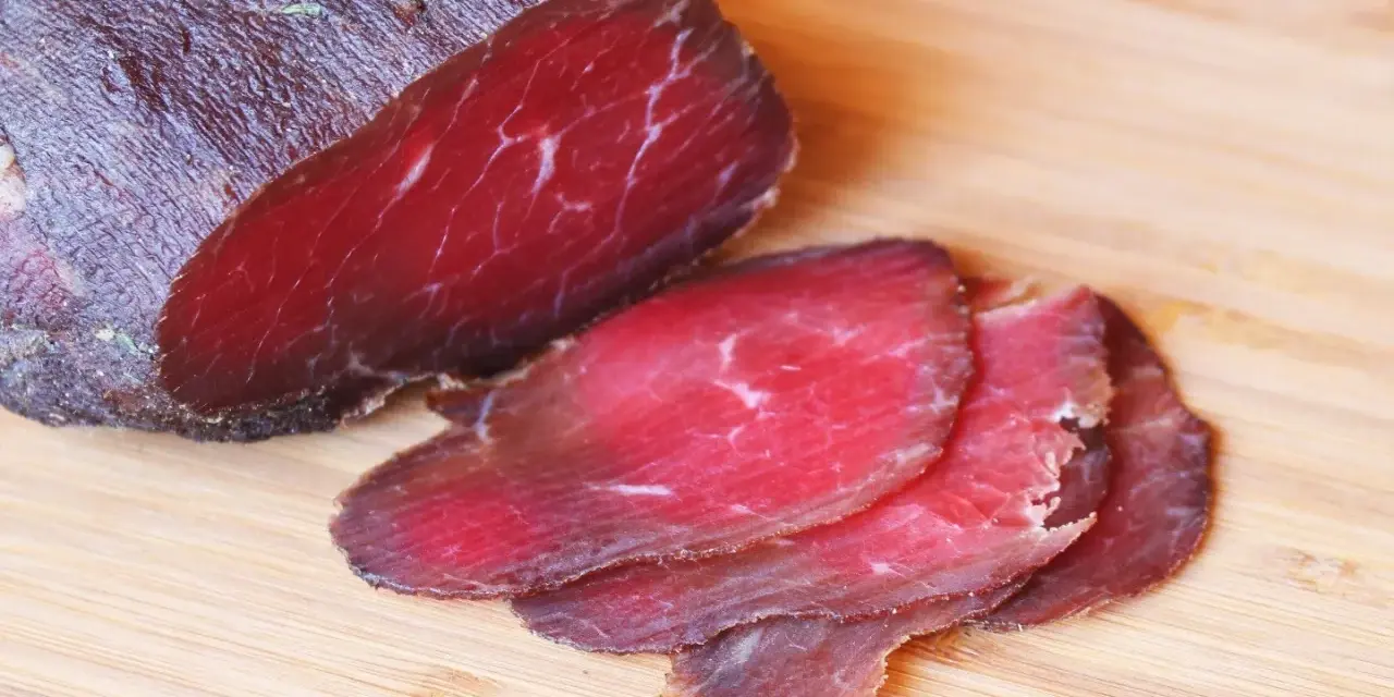Bresaola co to? Ciemnoczerwone, cienko pokrojone plastry suszonej wołowiny na desce.