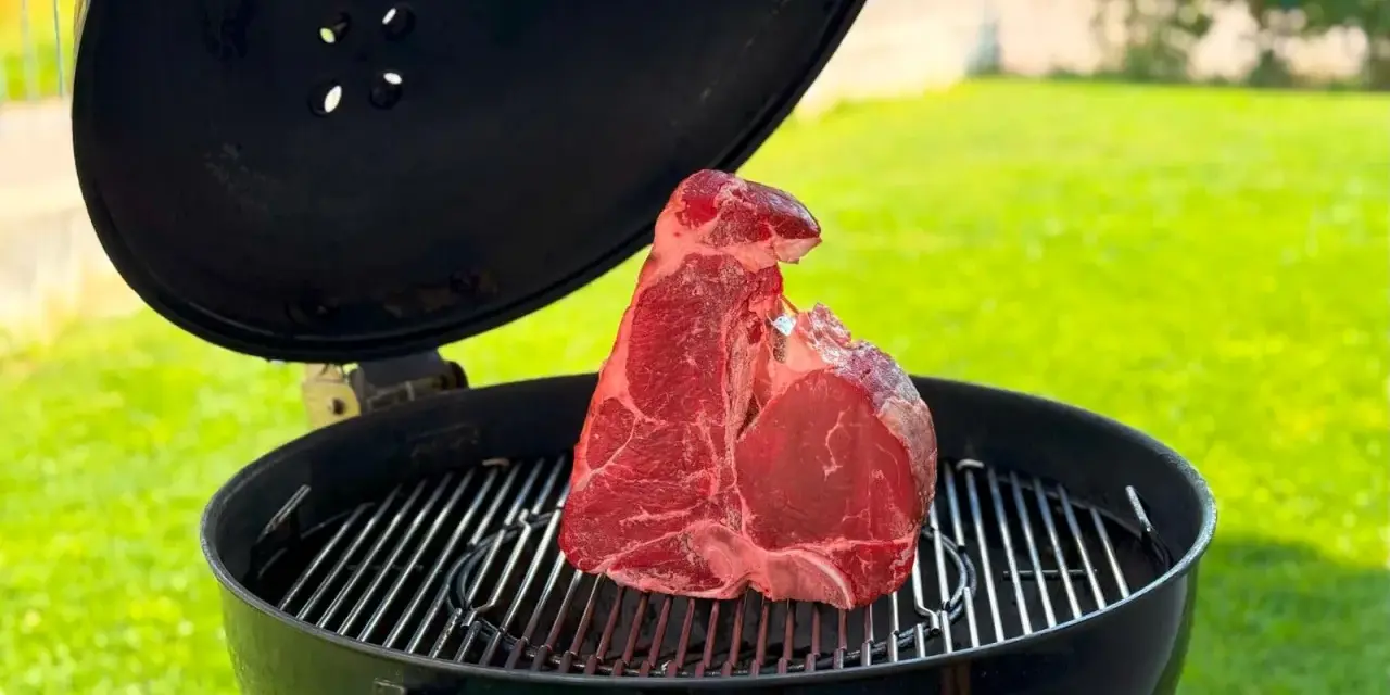 Una succulenta bistecca fiorentina cruda riposa sulla griglia di un barbecue, pronta per essere cucinata all'aperto.