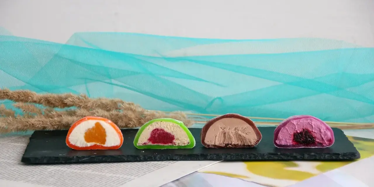 Cztery kolorowe mochi: pomarańczowe, zielone z malinami, czekoladowe i fioletowe z jagodami. Różne rodzaje słodkości.