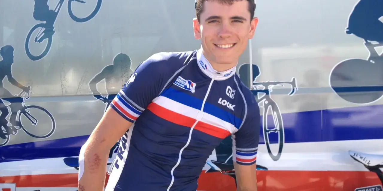 David Gaudu, a French cyclist, smiles in his team's blue, white, and red jersey, with bike graphics on the vehicle behind him.