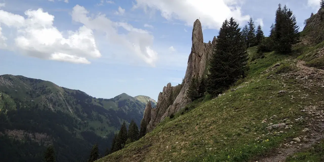 Ein steiler Bergpfad führt am markanten Siplinger Kopf vorbei, umgeben von grünen Hängen und Nadelbäumen.