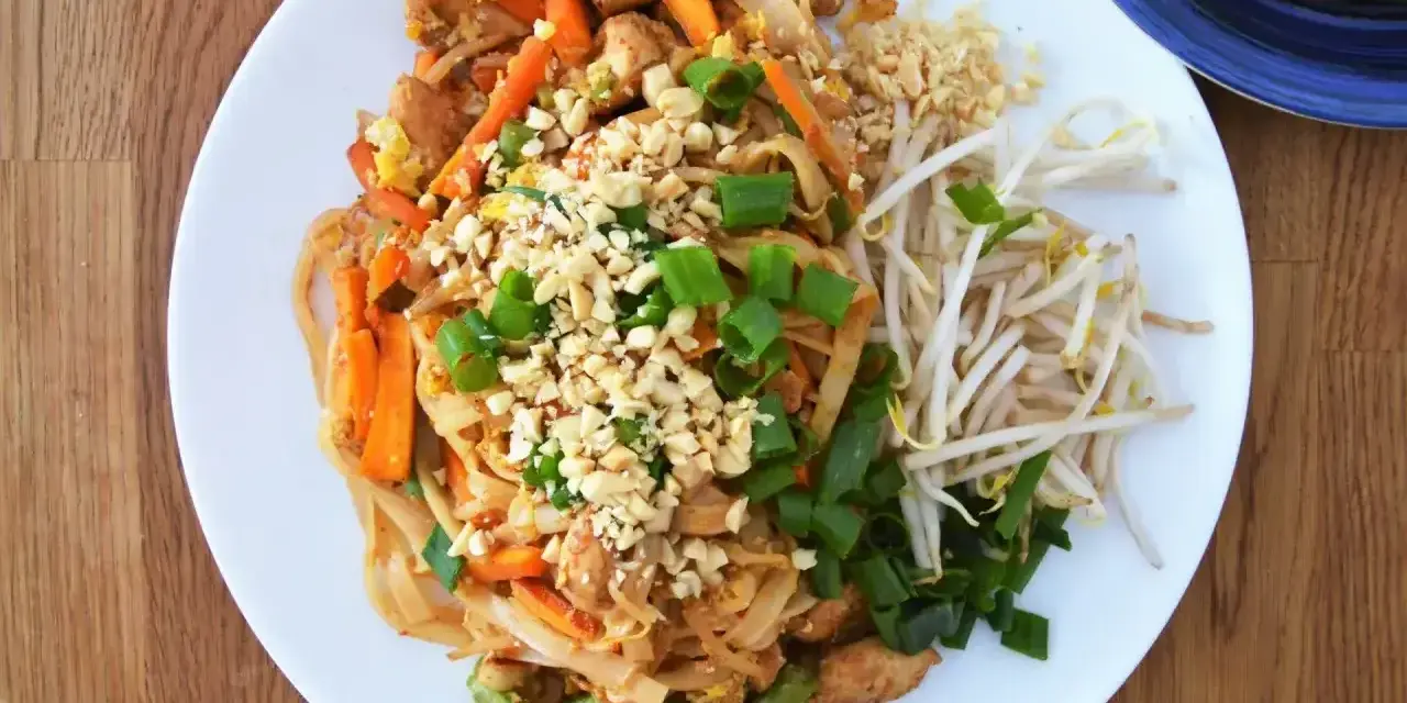 Pyszny sos pad thai z kurczakiem, warzywami i orzeszkami ziemnymi, podany z kiełkami fasoli mung.