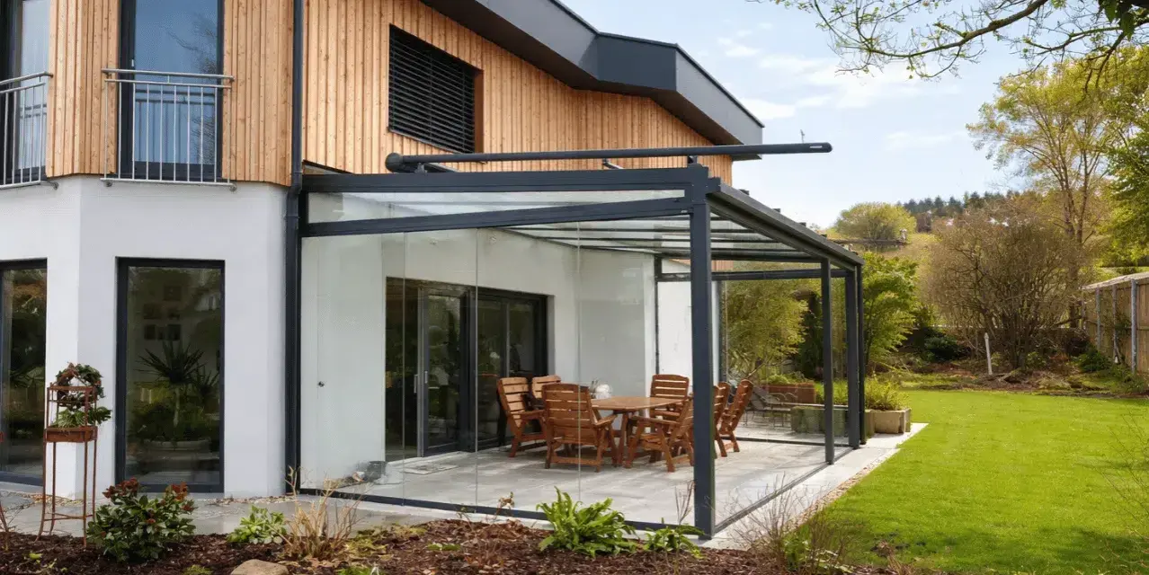 Moderne Glasdach-Terrasse mit Holztisch und Stühlen. Nachteile wie Hitzeentwicklung im Sommer sind zu bedenken.