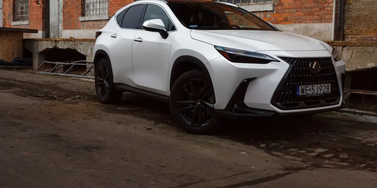 Biały Lexus 350h z czarnymi felgami stoi przed starą ceglaną budowką.