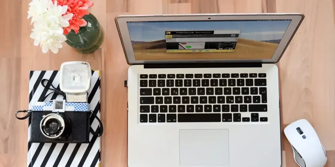 Jak zgrać zdjęcia z aparatu na laptop? Na biurku leży aparat, laptop i myszka.