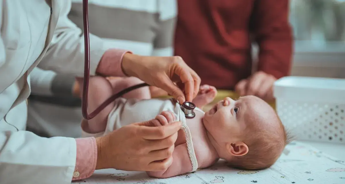 Pielęgniarka środowiskowa po porodzie osłuchuje noworodka. Rodzice obserwują badanie.