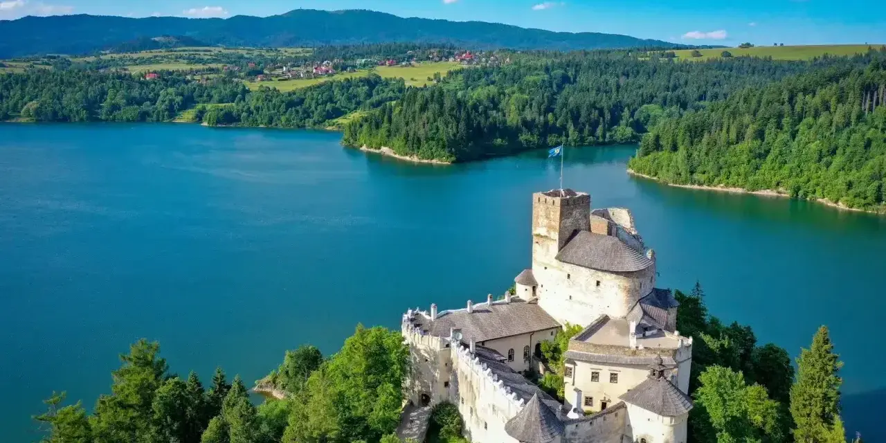 Zamek w Niedzicy góruje nad turkusowym zalewem czorsztyńskim, otoczony zielonymi lasami i górami.