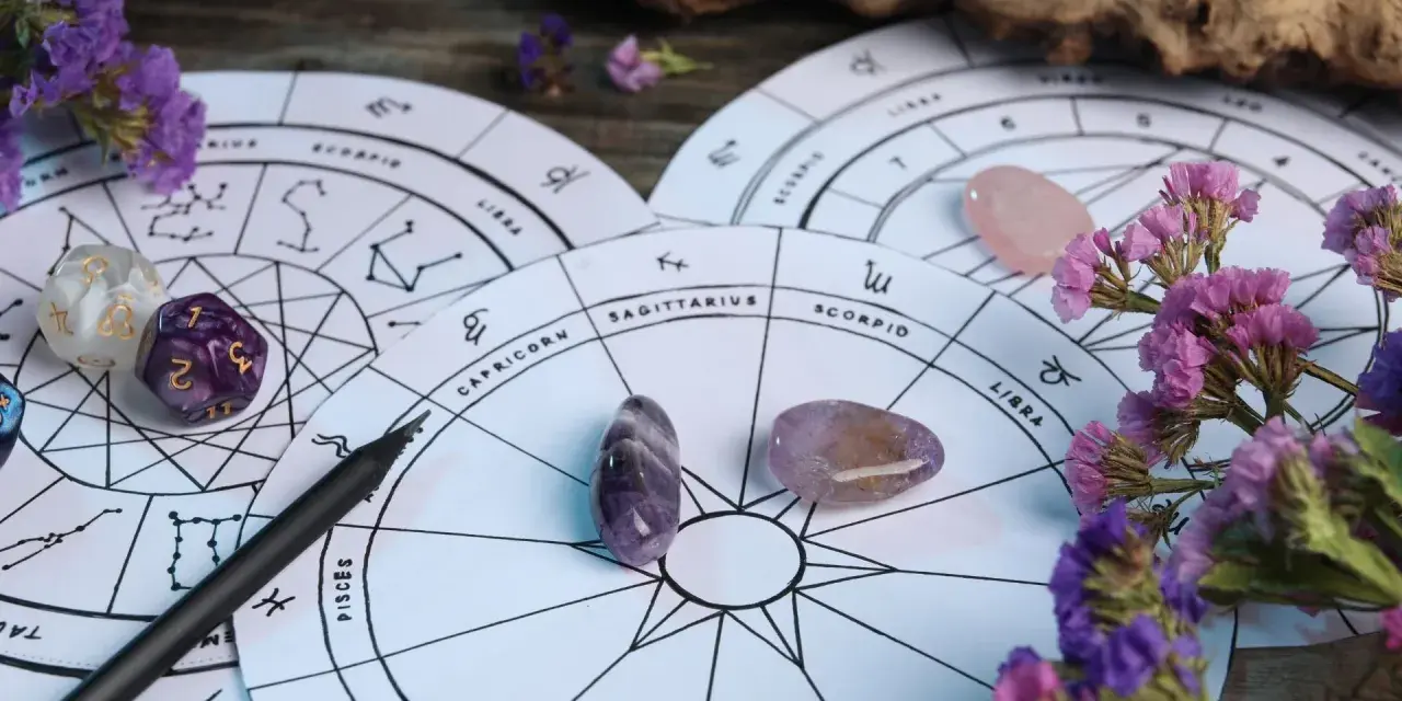 Astrologiczne koła zodiaku, kamienie, kostki i fioletowe kwiaty. 27 wrzesień znak zodiaku to Waga, symbolizująca równowagę.