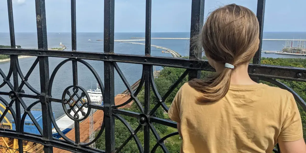 Dziewczynka podziwia widok z najwyższej latarni morskiej w Polsce. Widać morze, port i statki.