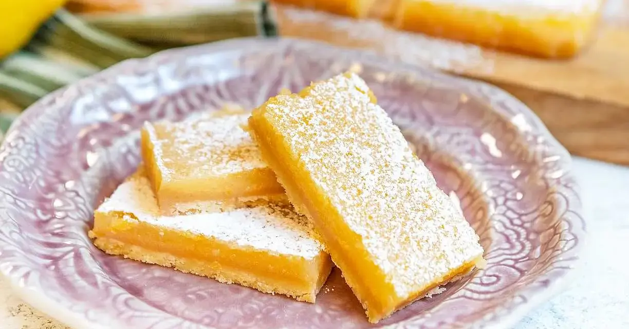 Citronkaka i långpanna, pudrad med florsocker, ligger upplagd på en vacker lila tallrik.