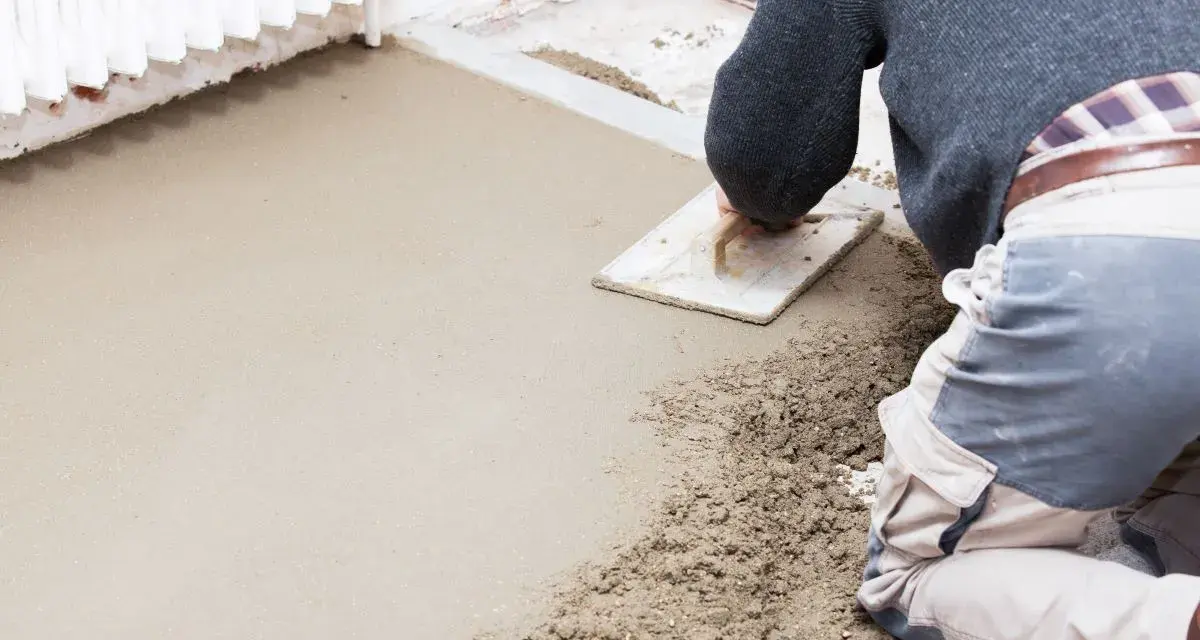 Operaio al lavoro con una cazzuola, livella il cemento per aumentare l'altezza del pavimento.
