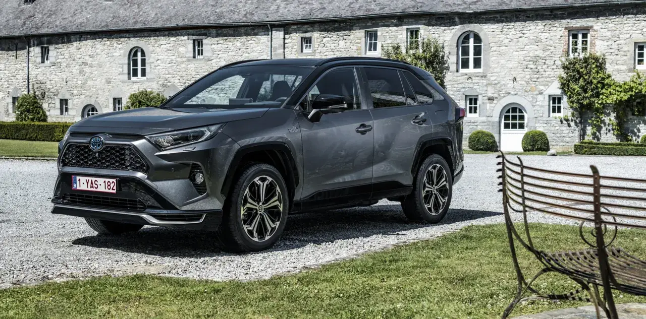 Szary Toyota RAV4 Hybrid przed kamiennym budynkiem. Zastanawiasz się, ile kosztuje Toyota RAV4 Hybrid?
