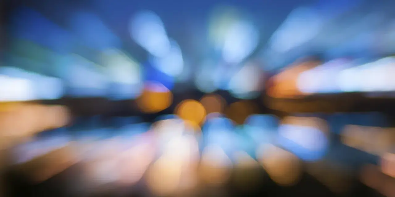 Luci sfocate di una città di notte, come se vedo sfocato da un occhio. Colori blu, arancioni e bianchi si fondono in un effetto astratto.