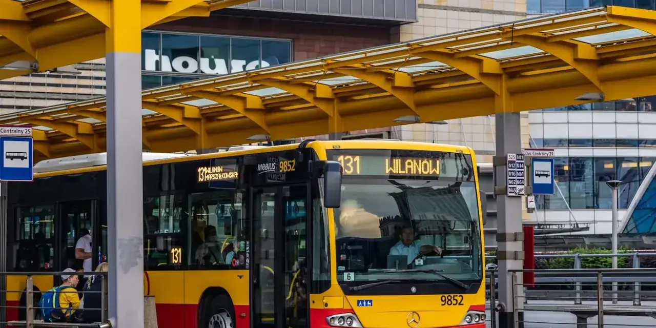 Żółto-czerwony autobus miejski na przystanku. Kierowca autobusu, jak i pasażerowie, zastanawiają się, ile zarabia kierowca autobusu.
