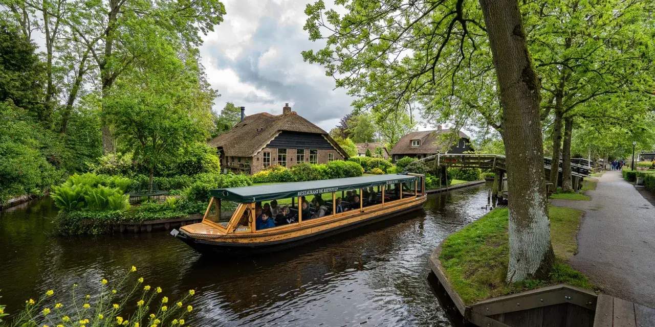 Bootfahrt durch Giethoorn, das Venedig der Niederlande. Grüne Ufer, Reetdachhäuser und gelbe Blumen am Wasser.