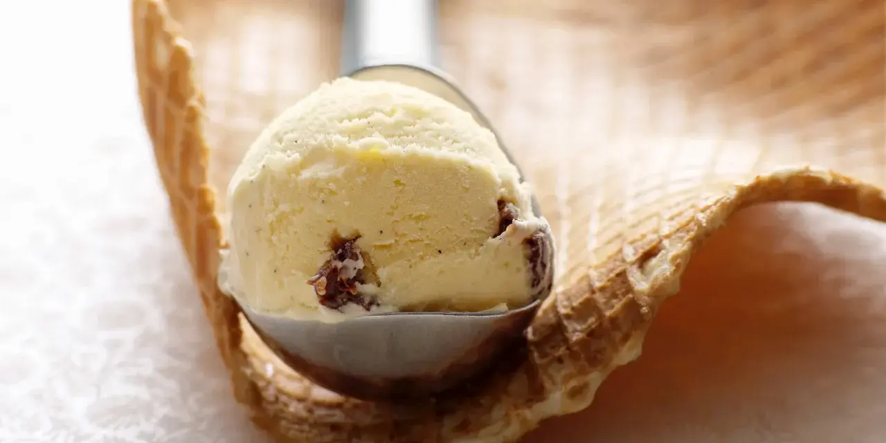 Ein Löffel cremiges Eis mit Rosinen und einem Hauch Rum ruht auf einem Waffelrand.
