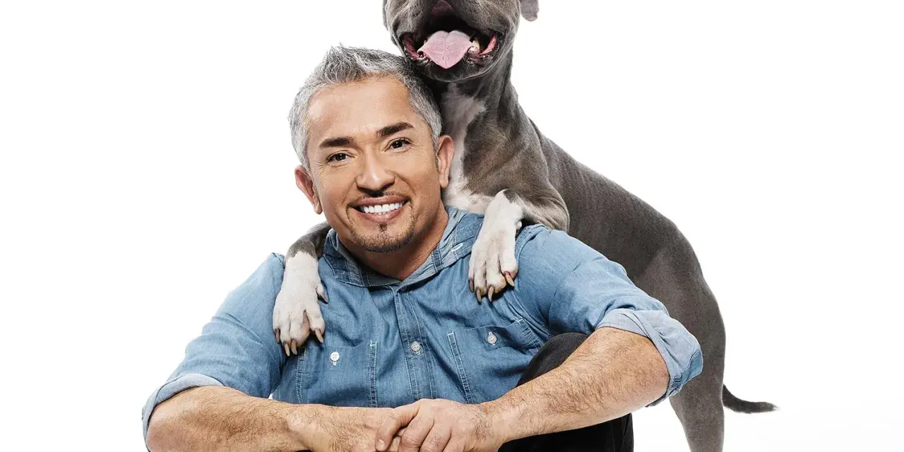 Cesar Millan z uśmiechniętym psem, który kładzie mu łapy na ramionach.