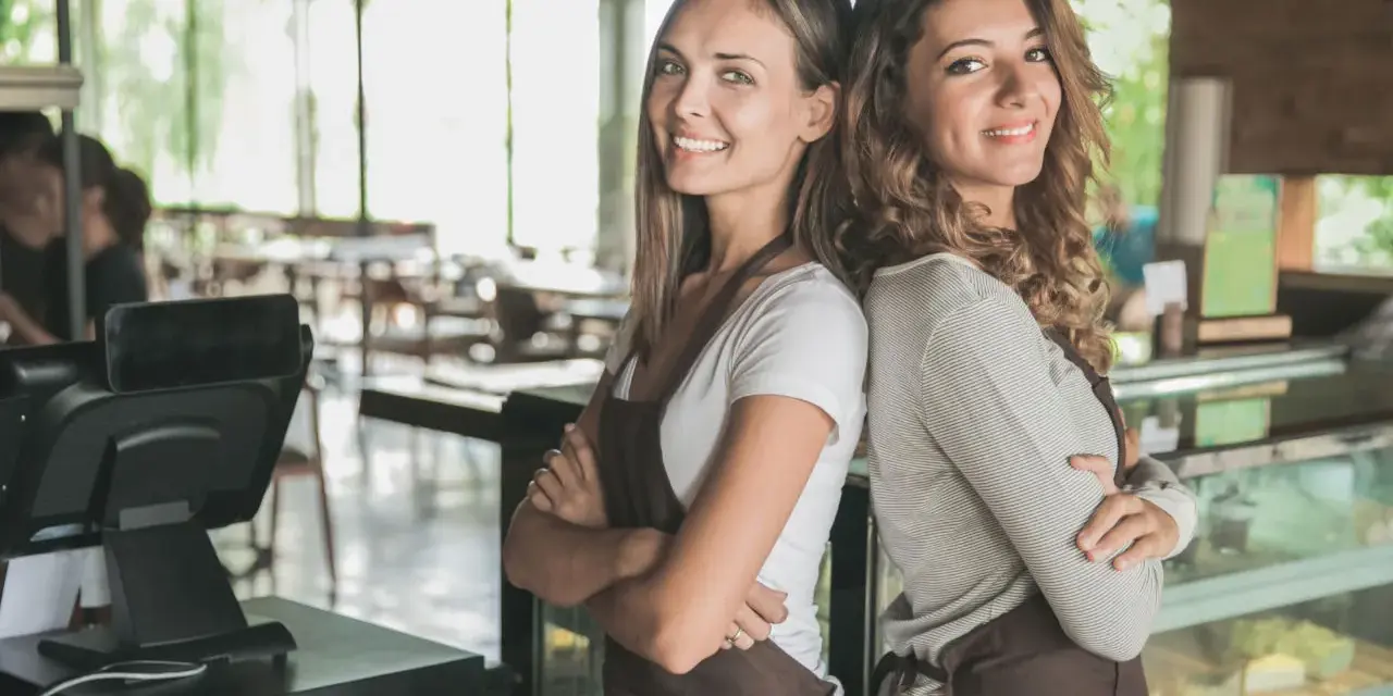 Dwie uśmiechnięte pracownice kawiarni, gotowe do obsługi. Od ilu lat można pracować w gastronomii? Odpowiedź znajdziesz w przepisach.