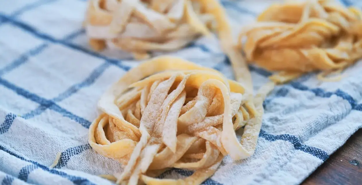 Świeże, domowe tagliatelle lub makaron spaghetti ułożone na lnianym ręczniku w kratkę.