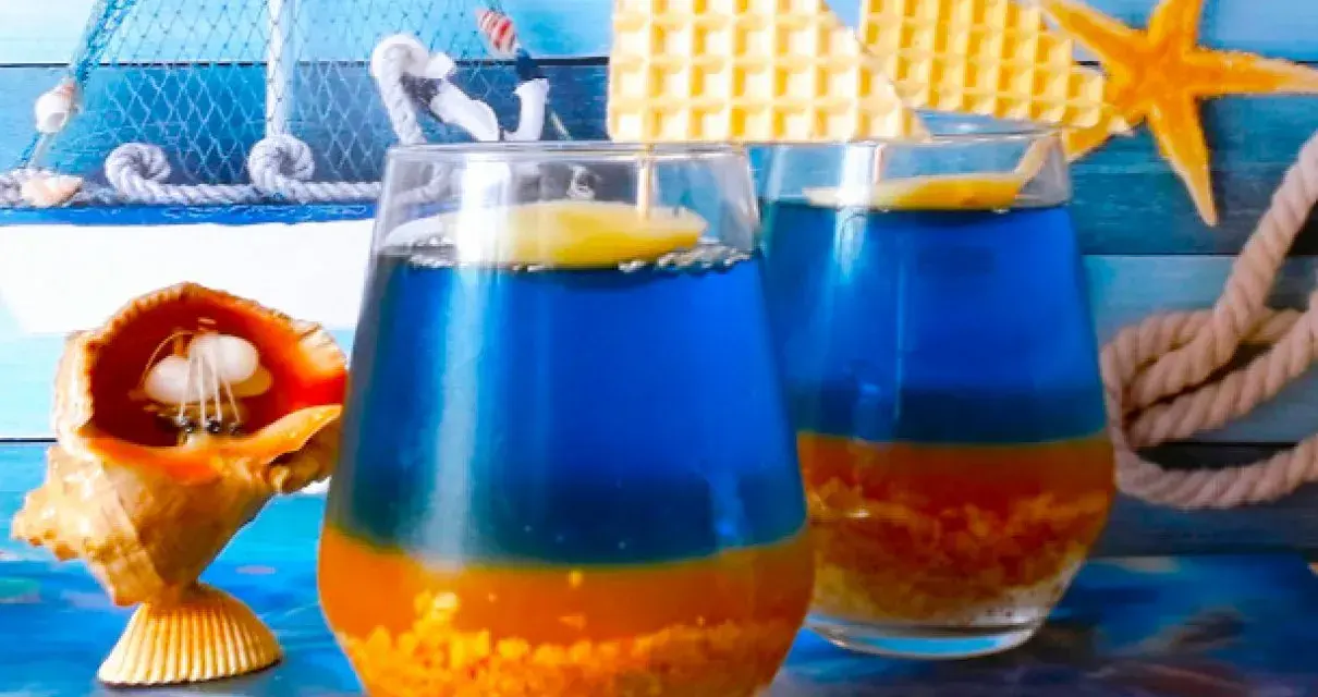 Dwa orzeźwiające drinki Błękitna Laguna, ozdobione plasterkiem cytryny, na tle morskich dekoracji.