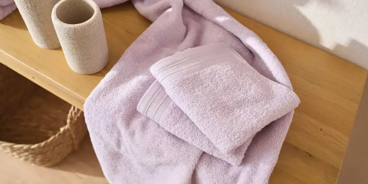 Variedad de tipos de toallas de baño en color lavanda, apiladas sobre una superficie de madera.