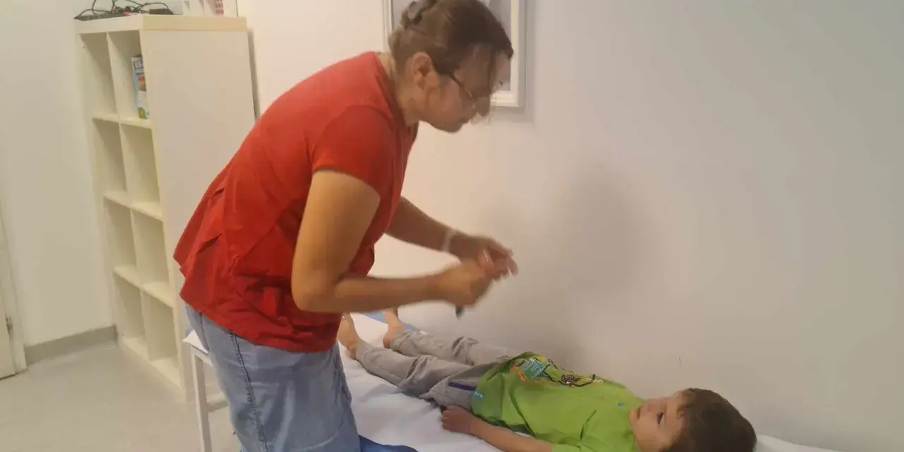 Lekarz bada chłopca leżącego na kozetce, oceniając objawy uszkodzonego układu nerwowego u dziecka.