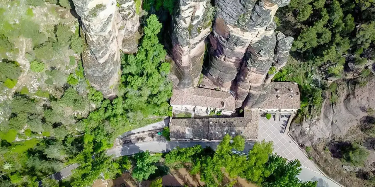 Vista aérea del **barranco de la Hoz, Guadalajara**, con edificios integrados en las rocas y vegetación exuberante.