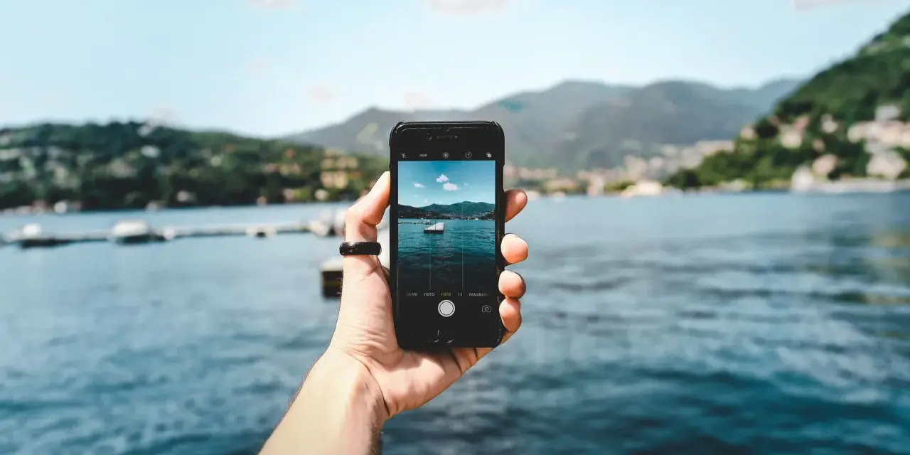 Dłoń trzyma smartfon, na ekranie którego widać zdjęcie jeziora z łódką. To przykład techniki photo stacking, która pozwala uzyskać niezwykłą głębię ostrości.