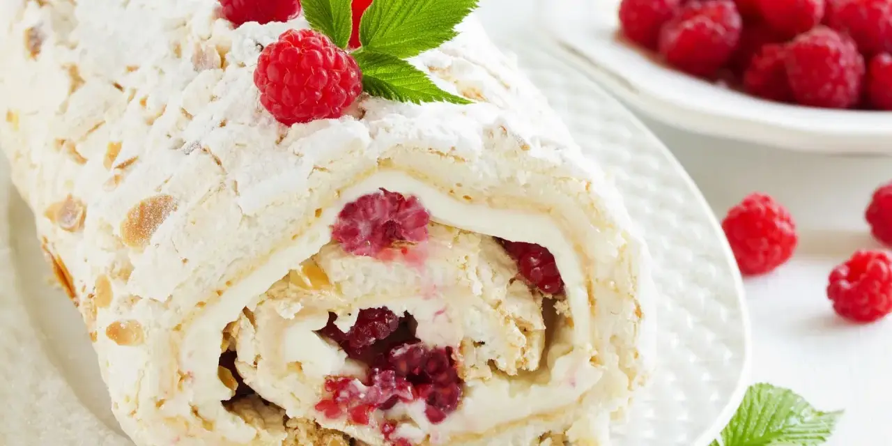Rolada bezowa z mascarpone i malinami, posypana cukrem pudrem i płatkami migdałów.