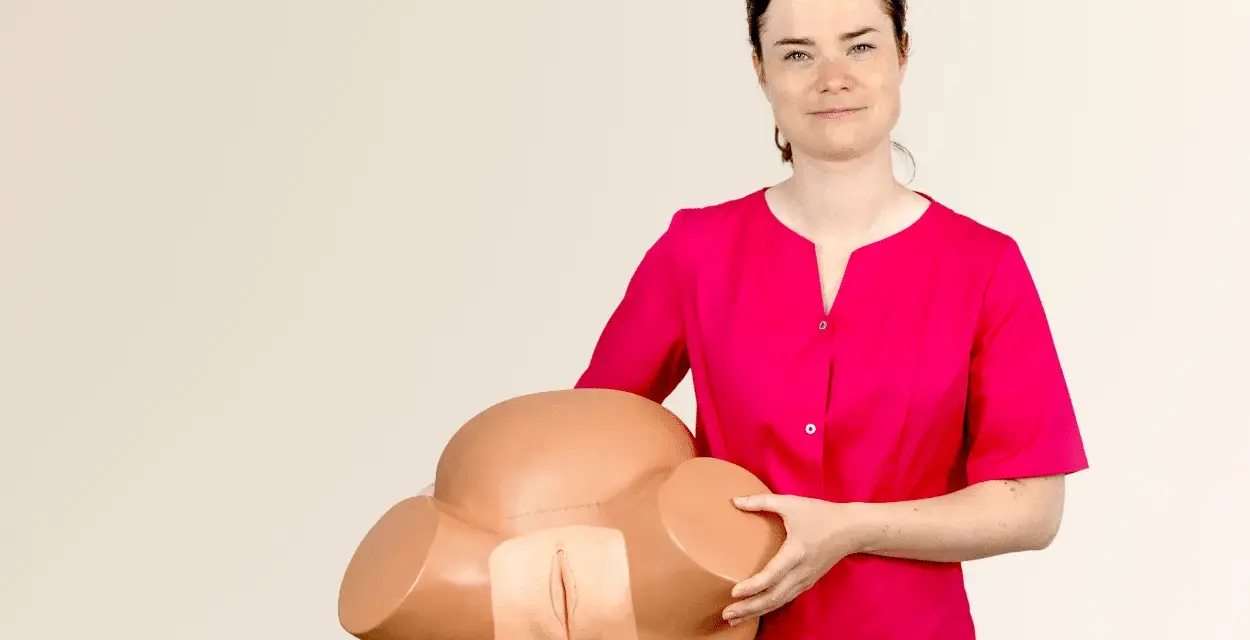 Kobieta w różowej bluzce prezentuje model miednicy do nauki masażu krocza przed porodem.