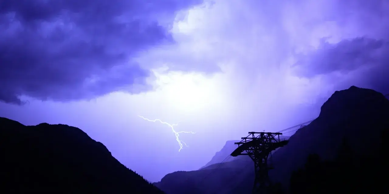 Un éclair zèbre le ciel violet d'un **orage en montagne que faire** ? Une cabine de téléphérique silhouette se dresse, témoin de la fureur de la nature.