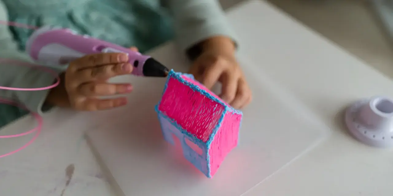 Dziecko tworzy domek z różowego i niebieskiego filamentu. Długopis 3d nie wciąga filamentu, ale tworzy trójwymiarowe dzieło.