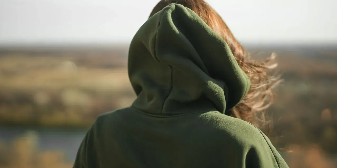 Osoba w zielonej bluzie z kapturem patrzy na krajobraz. Nie wiadomo, ile waży bluza z kapturem, ale wygląda na ciepłą.