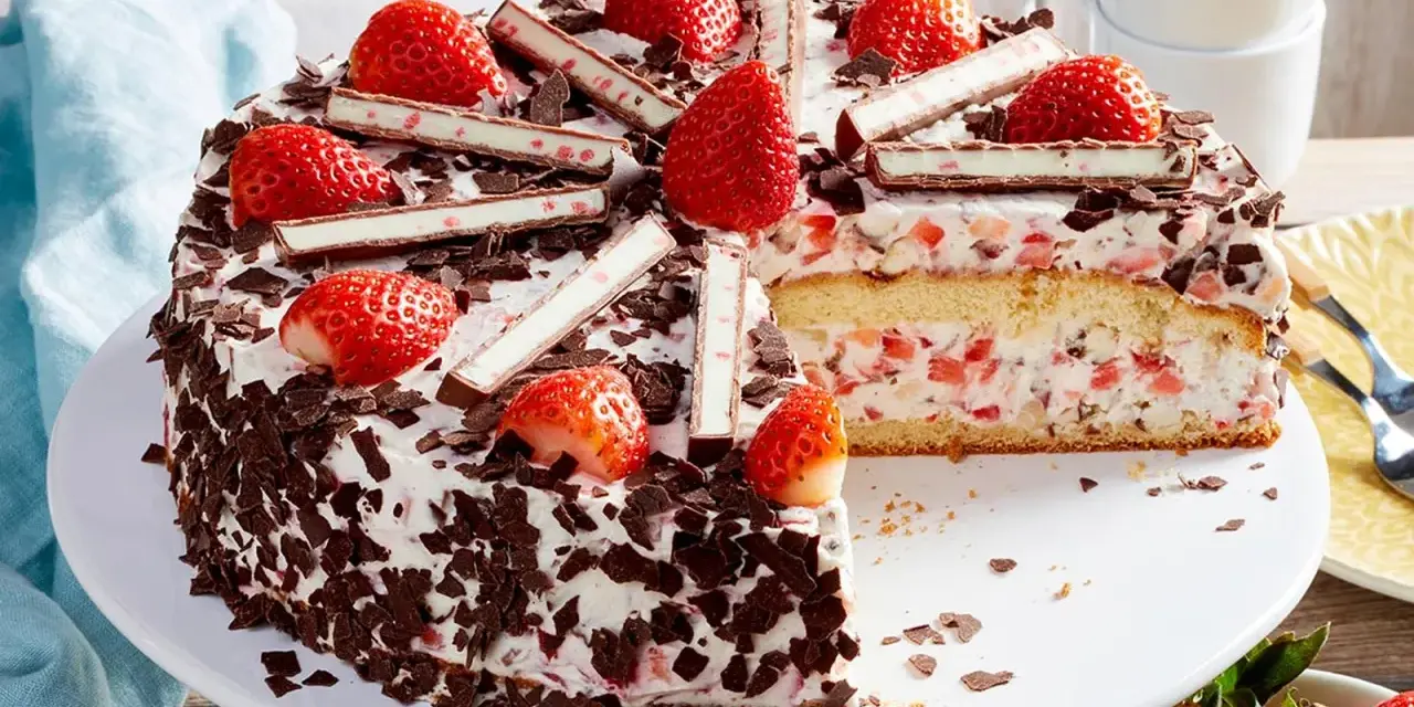 Eine köstliche Yogurette Torte mit frischen Erdbeeren, Schokostückchen und Sahne. Ein Stück ist bereits angeschnitten.