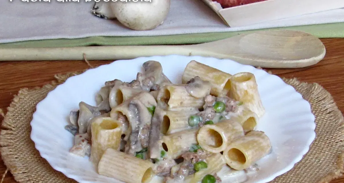 Piatto di pasta alla boscaiola con funghi, piselli e salsiccia, servita su un piatto bianco con una tovaglietta di juta.
