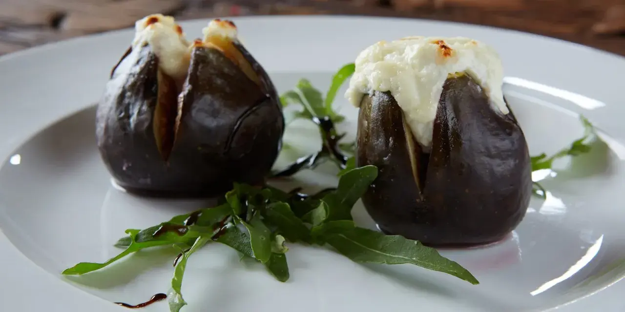 Zwei gefüllte Feigen, die auf einem Teller mit Rucola und Balsamico-Glasur liegen. Ein köstliches Gericht, das zeigt, wie man Feigen grillen kann.