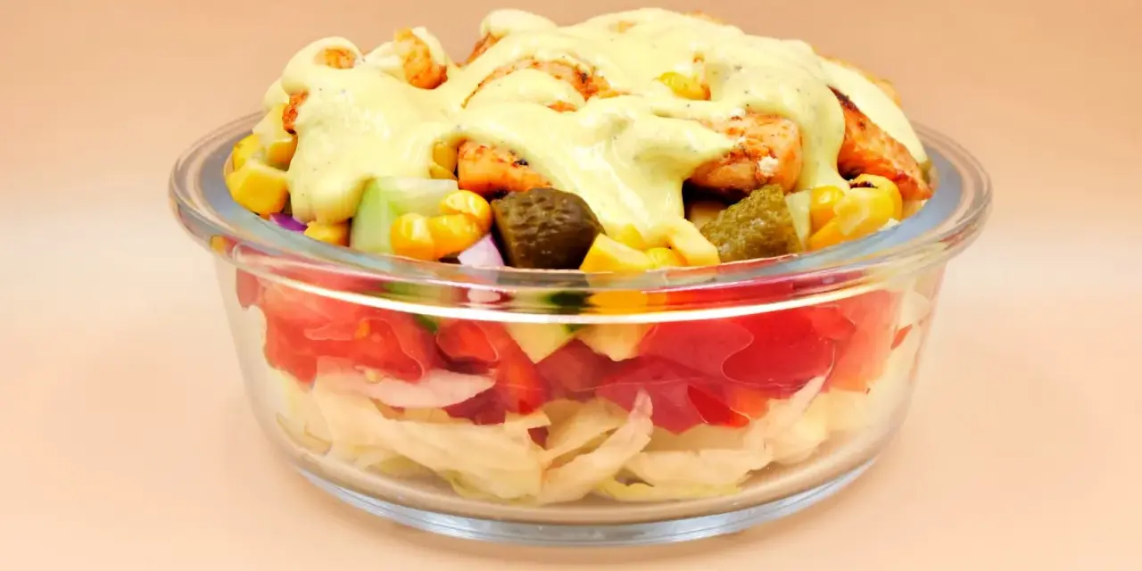 Sałatka gyros w szklanej misce z kurczakiem, kukurydzą, ogórkiem i sosem.