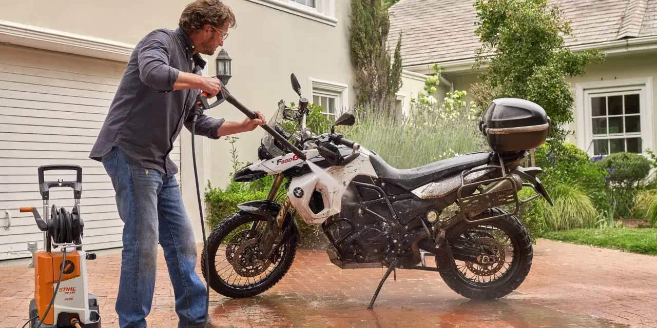 Uomo lava moto a idropulitrice in giardino. Ecco come lavare la moto a casa per mantenerla splendente.
