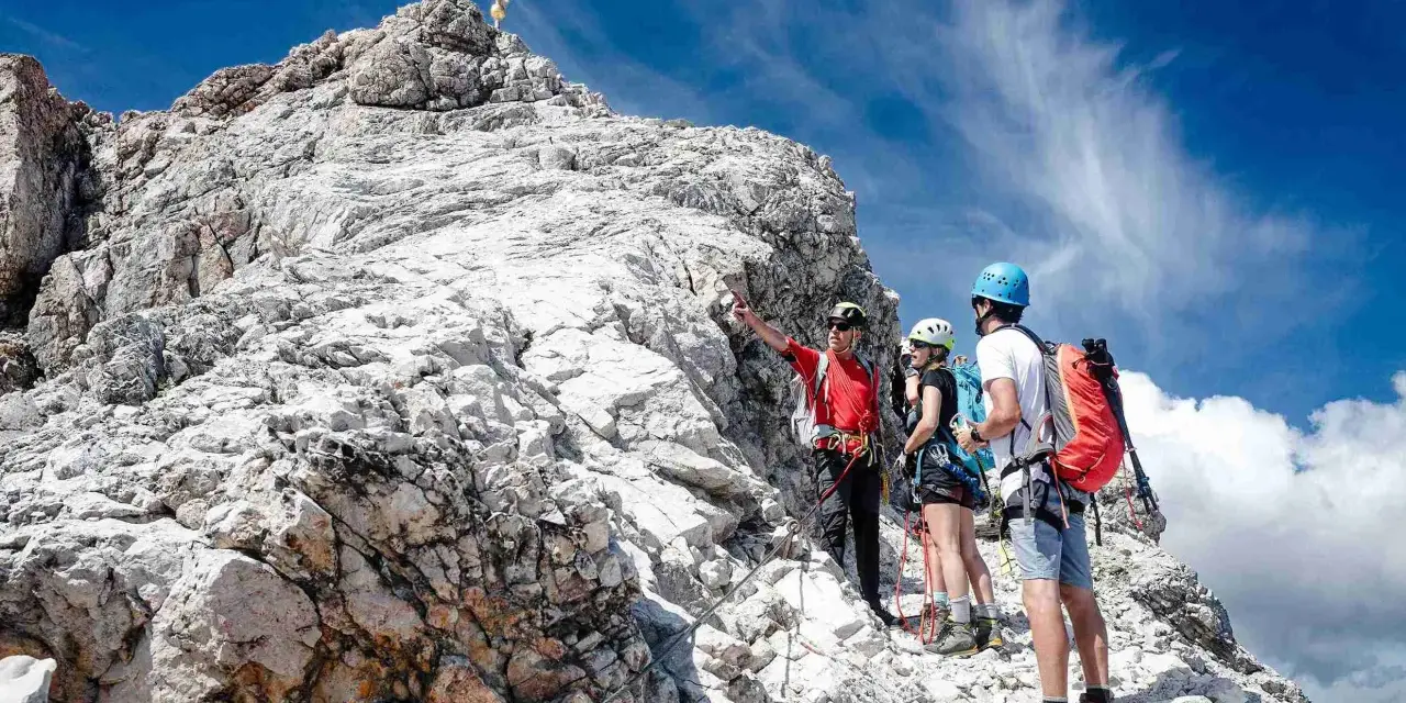 Bergsteiger am Gipfel der Zugspitze ohne Klettersteig. Ein Führer erklärt den Weg.
