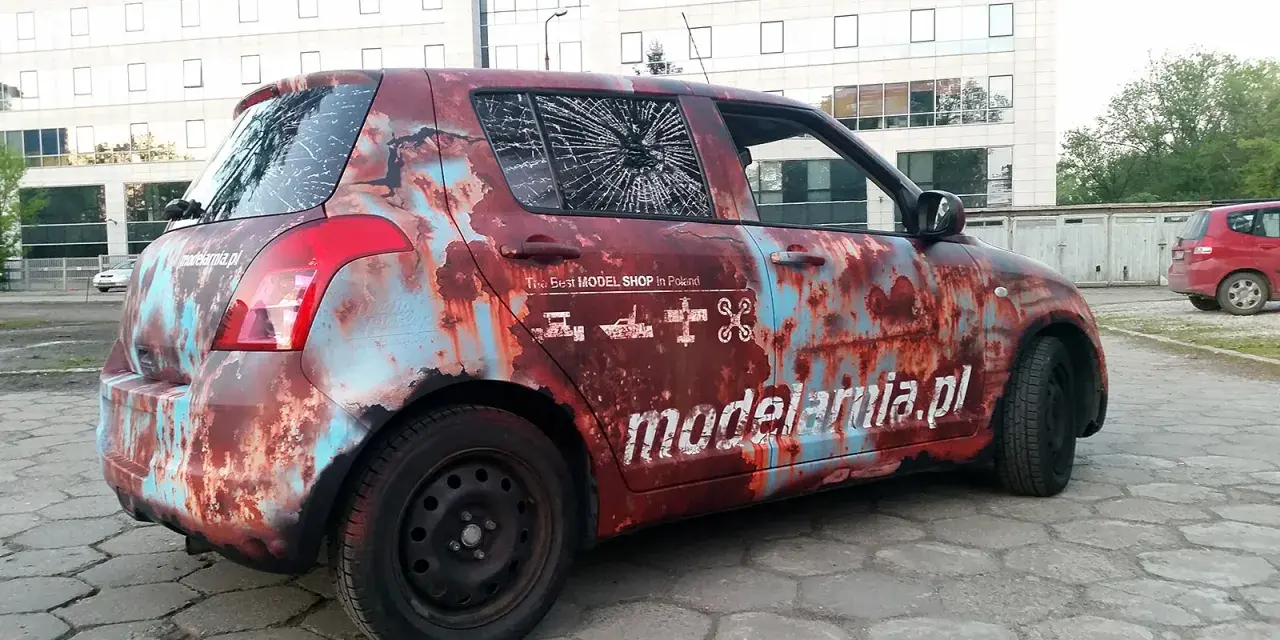 Samochód z okleiną imitującą rdzę, z napisem "modelarnia.pl" i ikonami modeli. Reklama na samochodzie zarobek.