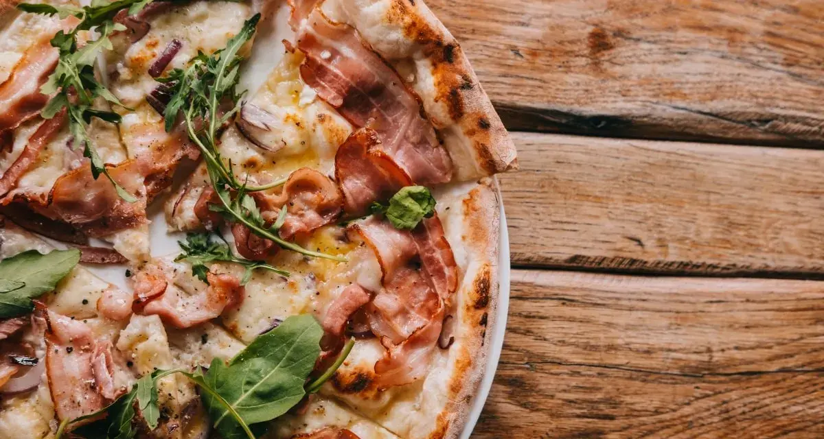 Pyszna pizza carbonara z chrupiącym boczkiem i rukolą na drewnianym stole.