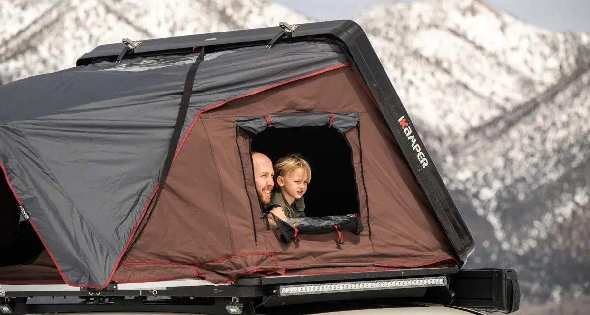 Vater und Kind schauen aus einem Dachzelt. Ein Abenteuer im Winter mit dem Dachzelt ist möglich.