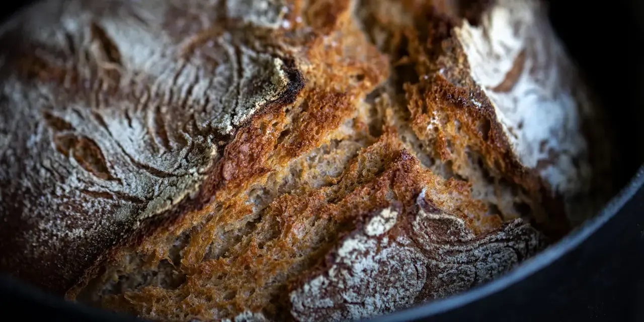 Frisch gebackenes Brot mit knuspriger Kruste ruht auf Backpapier im Gusseisentopf.