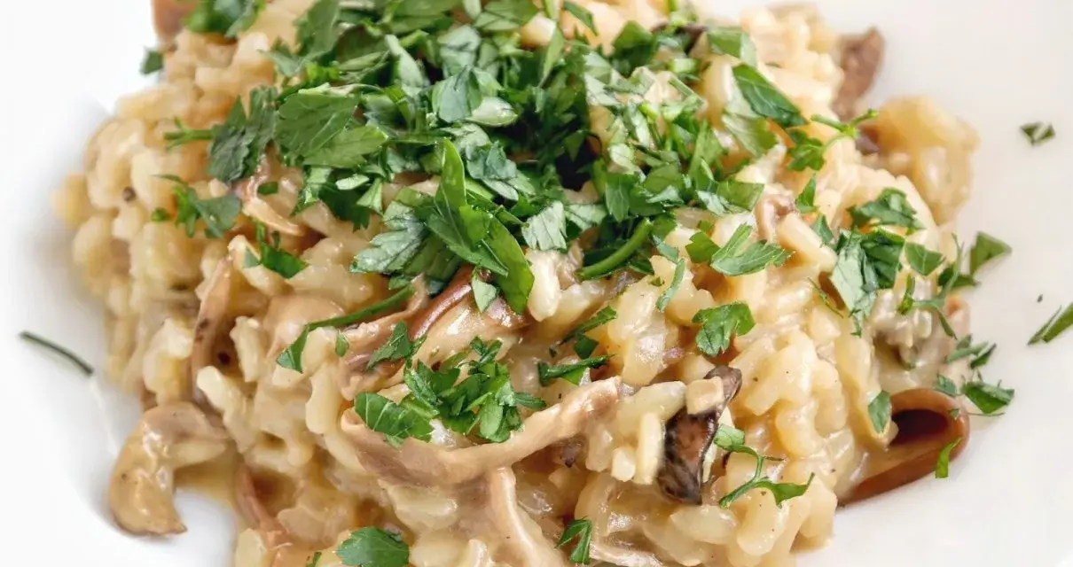 Kremowe risotto z grzybami, posypane świeżą natką pietruszki, wygląda apetycznie.