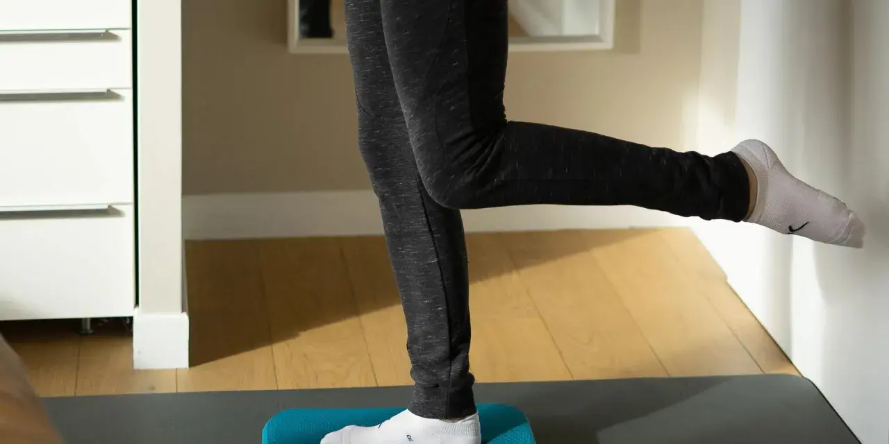 Personne effectuant des exercices de renforcement de la cheville sur un step bleu, idéal pour la rééducation après une entorse.