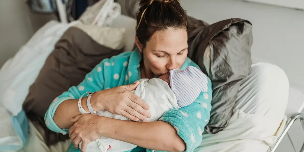 Mama tuli dziecko po cesarce, czule całując je w czapeczkę. Laktacja po cesarce może być wyzwaniem, ale miłość jest silniejsza.